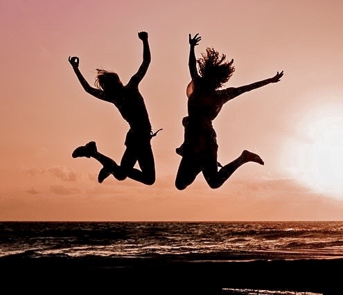 2 people jumping on the beach at sunset