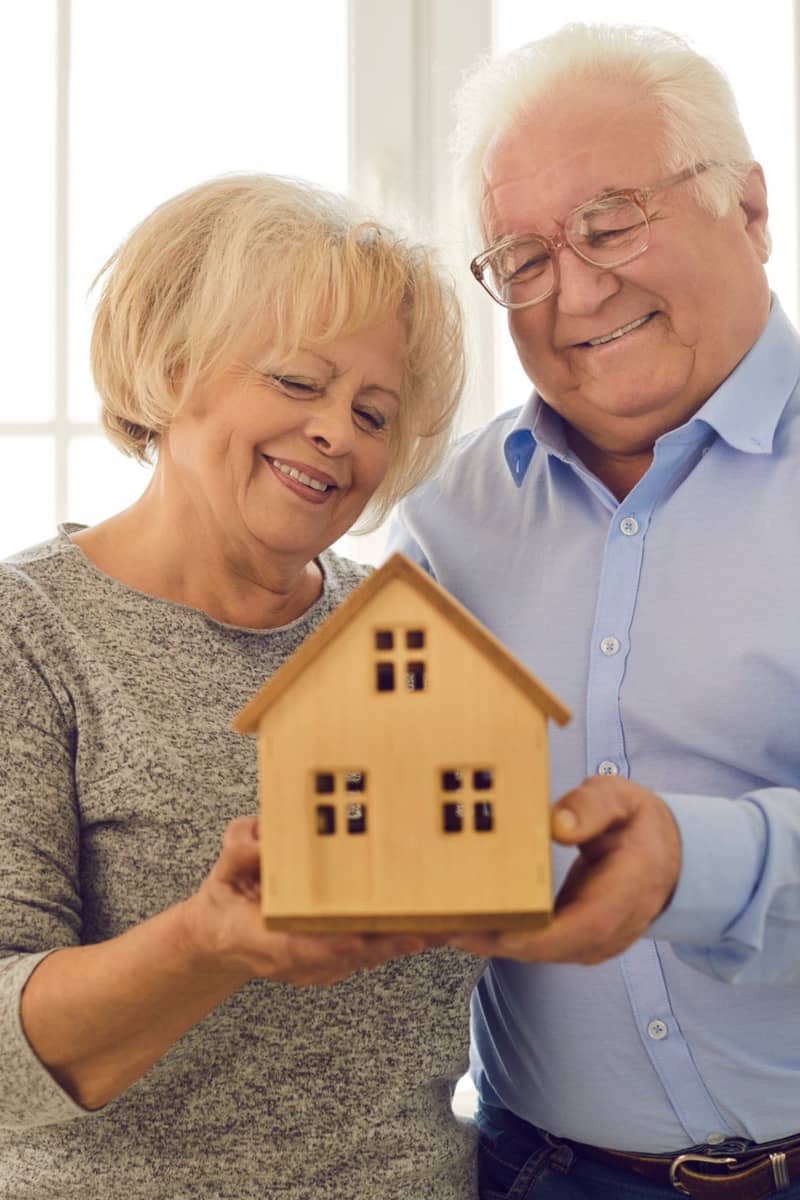a couple holding a toy house seemingly very happy with themselves