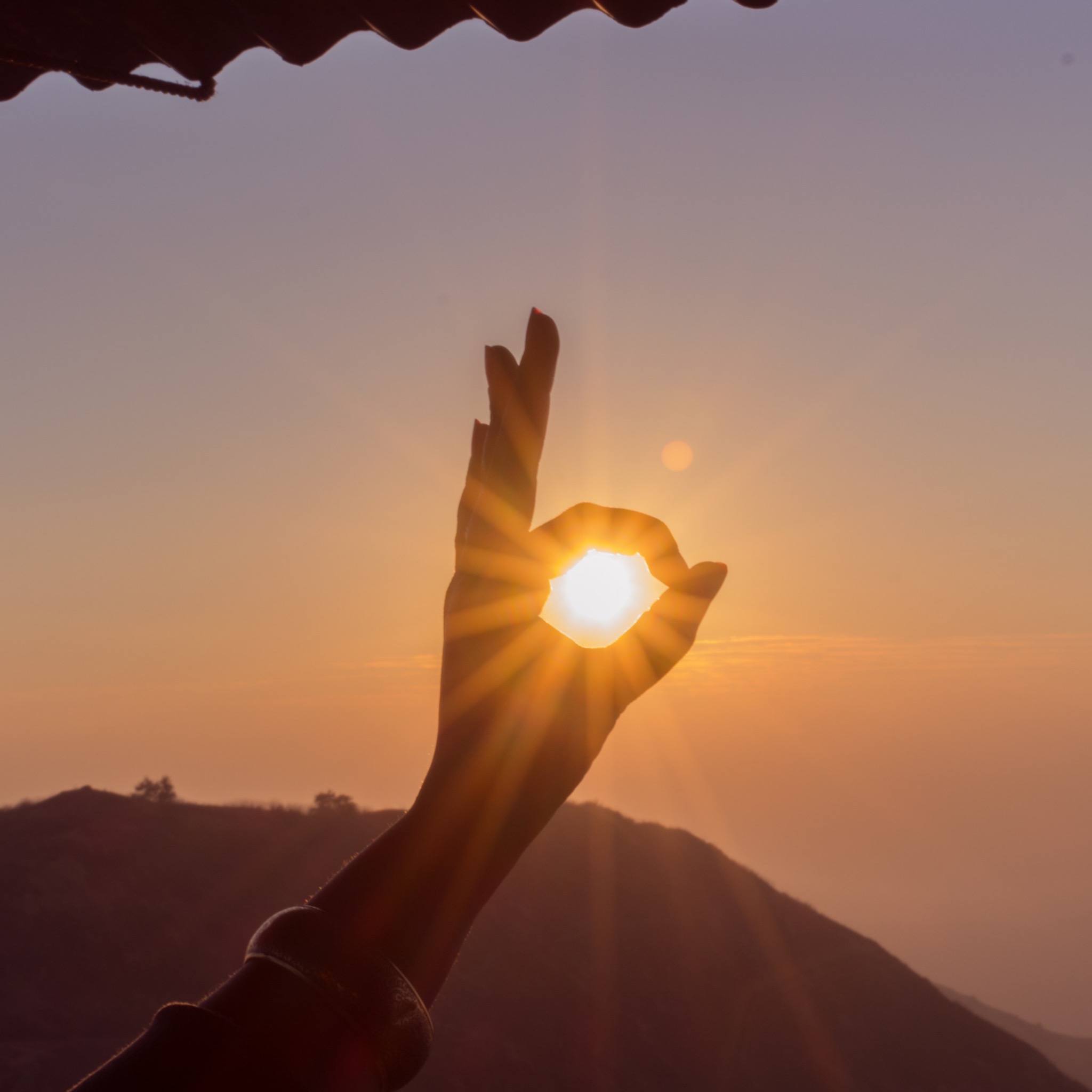 hand making an ok sign with the sun peering through the O