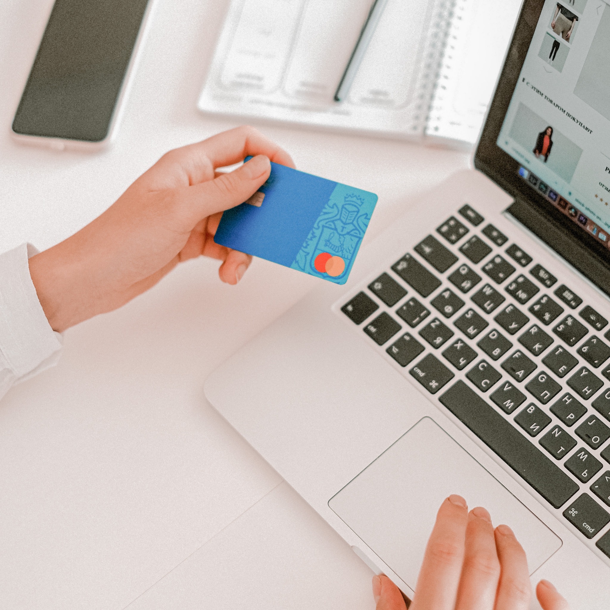 a persons hand holding a credit card above their open laptop to imply they are about to spend some money
