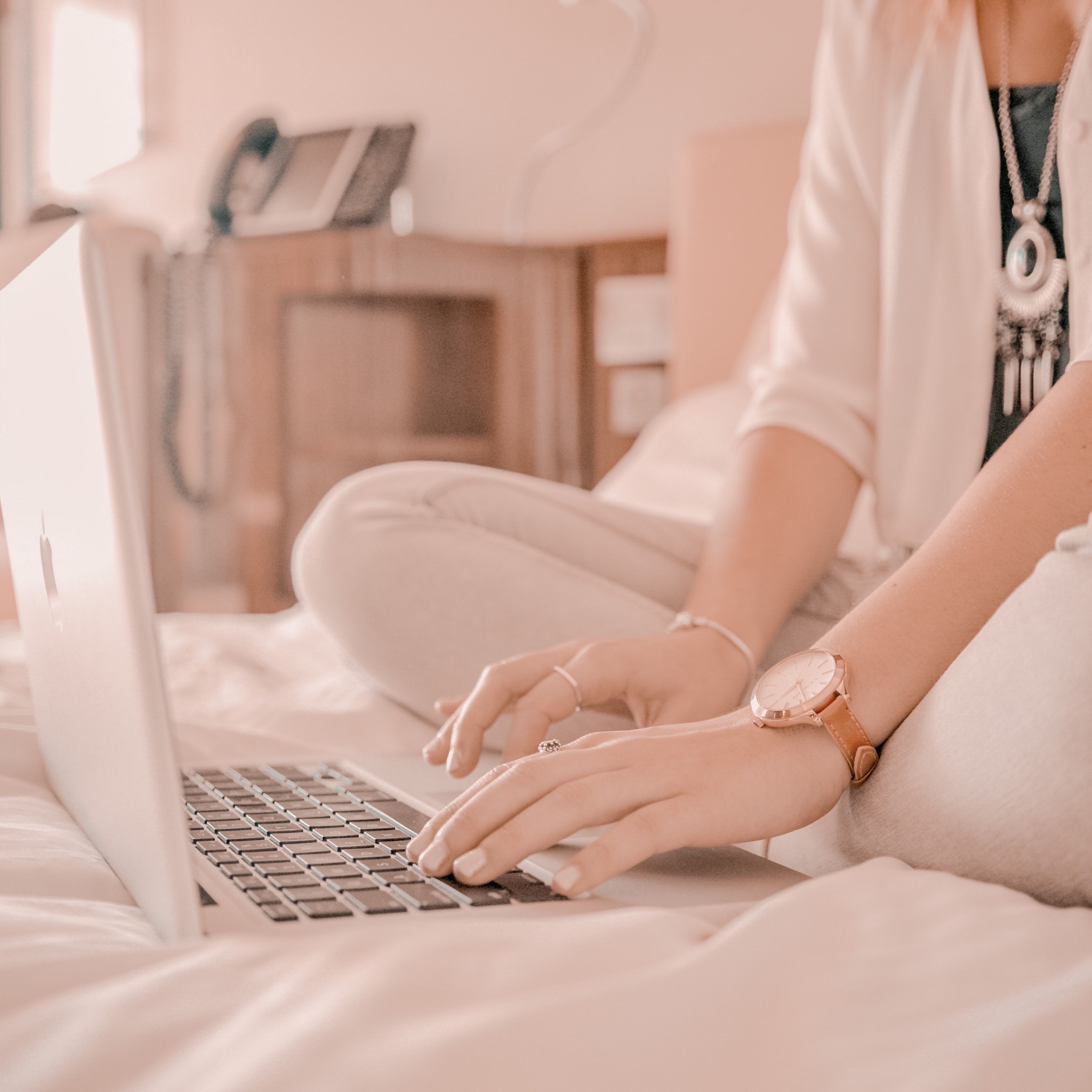 a lady sitting on a bed with her laptop in front of her with her hands on the keyboard stimulating typing