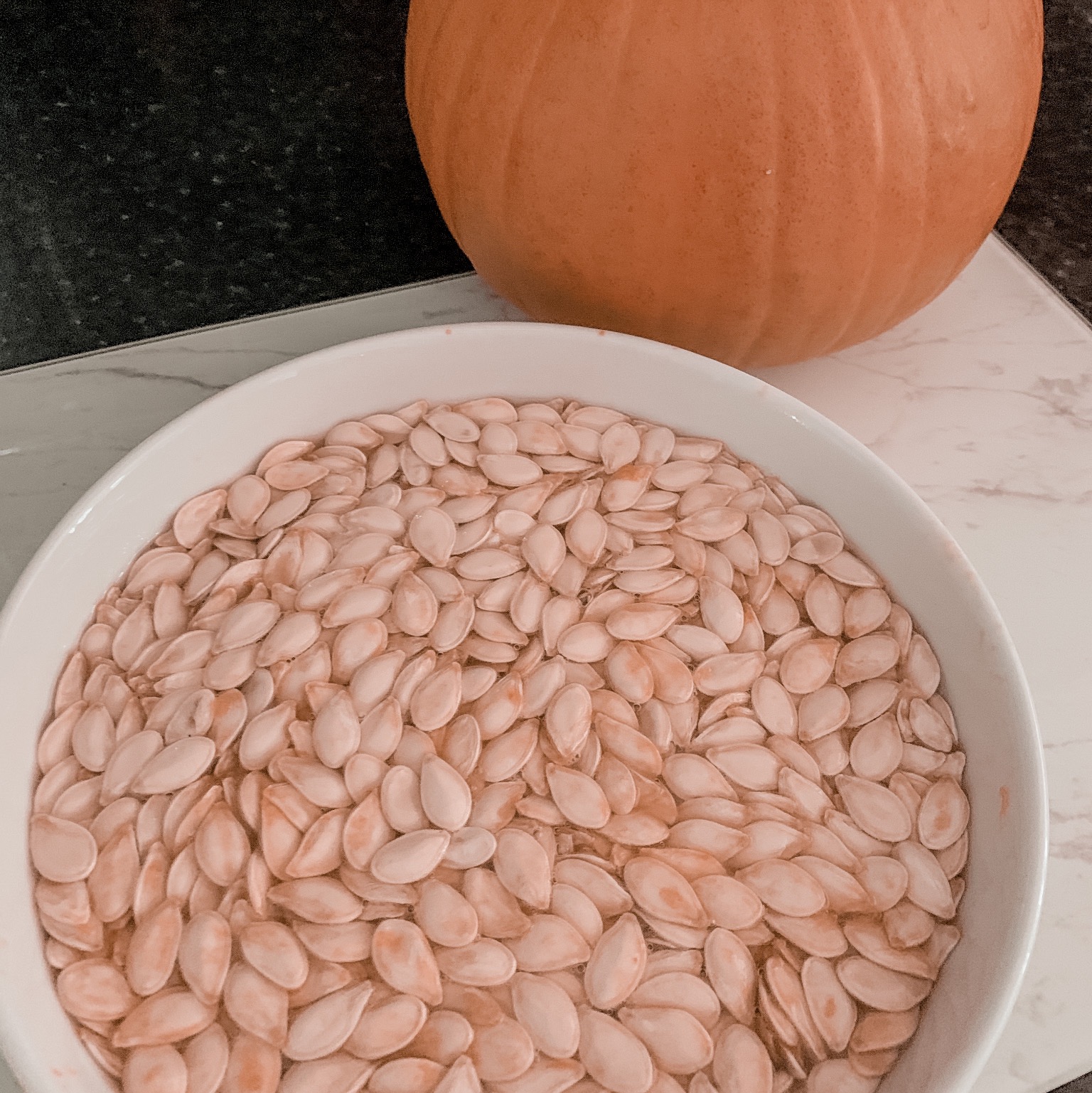 a bowl of pumpkin seeds with a pumpkin in the back ground