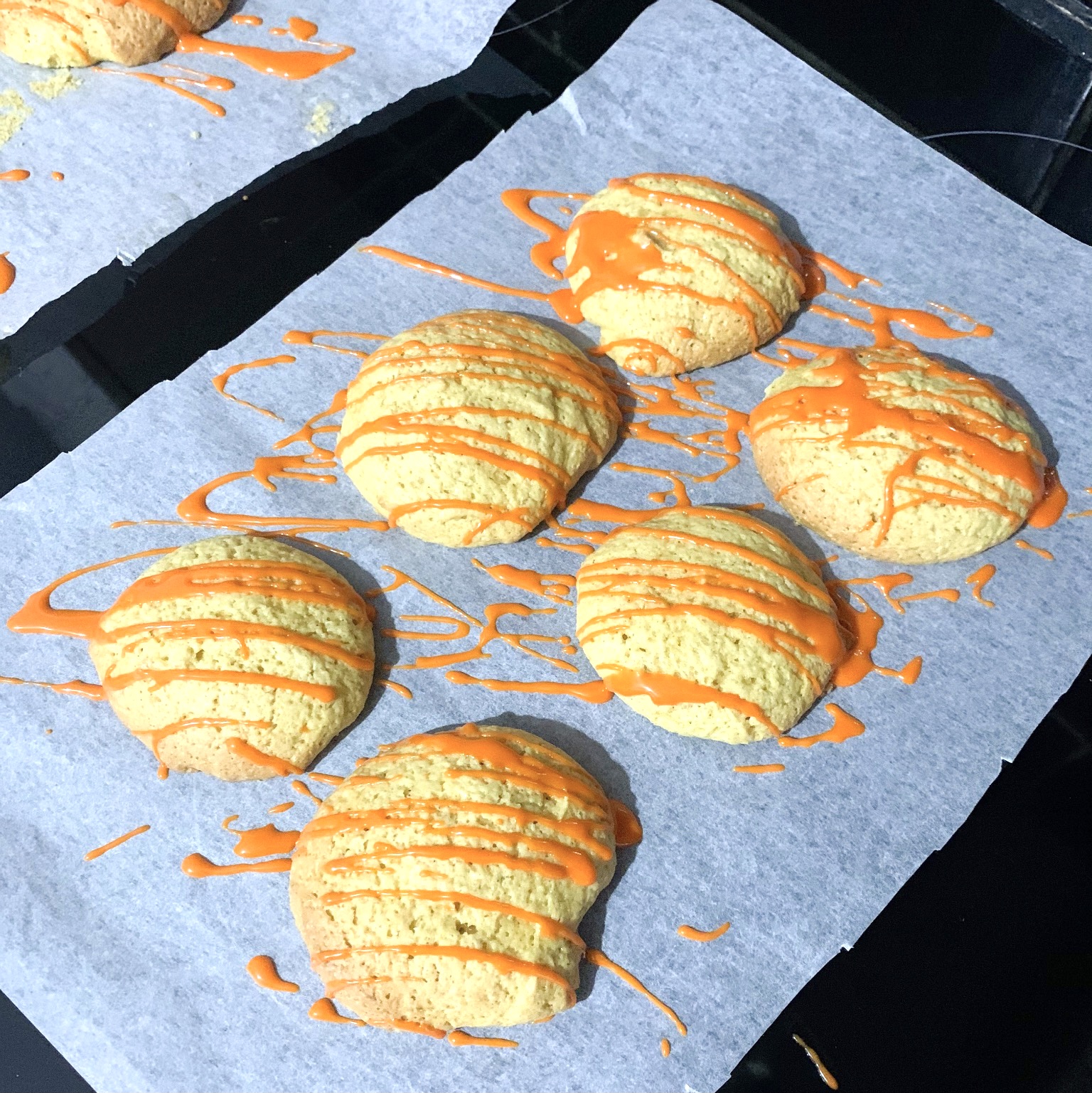 a baking tray with 6 pumpkin cookies with orange icing drizzled over them